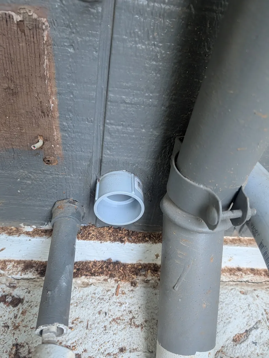 Close-up of the 2" PVC fitting tucked tight against the wall, sealed with silicone